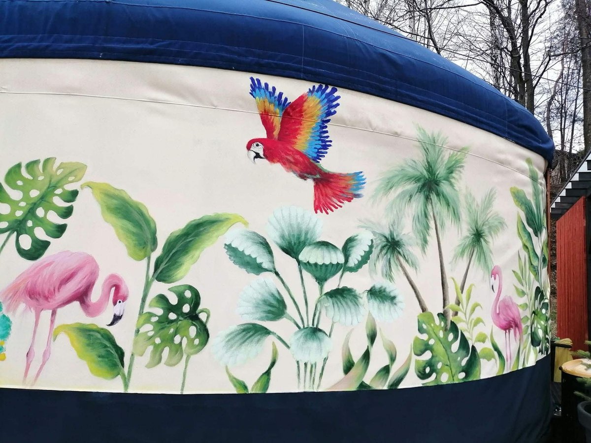 Kolorowy mural na cylindrycznej niebiesko-białej konstrukcji z papugą, flamingami, palmami i liśćmi monstery